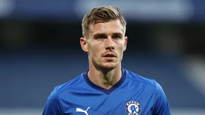 A mid-30s anonymous KFUM Oslo player in a solid blue jersey, head-and-shoulders shot, intense focus, blurred stadium...