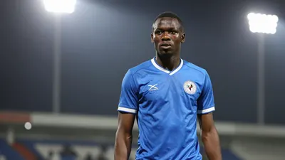 A 25-year-old Nigerian midfielder with a muscular build and short hair, wearing a solid blue jersey, photographed with an...